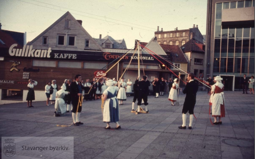 Folkedans på torget i Stavanger hvor folk i tradisjonelle drakter holder bånd rundt pinne
