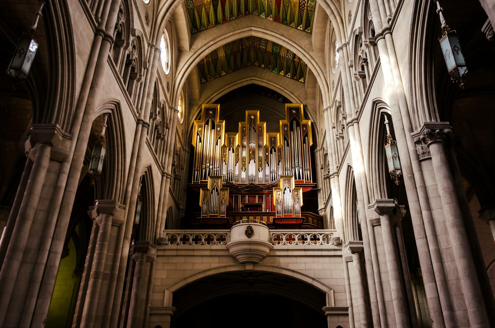 Stort majestetisk orgel i en utsmykket katedral eller kirke av stein, med gulldetaljer.