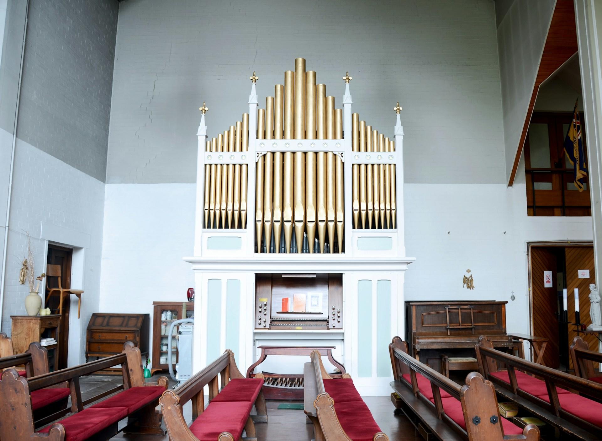 Hvitt og brunt orgel stående i et kirkerom ved siden av kirkebenkene.