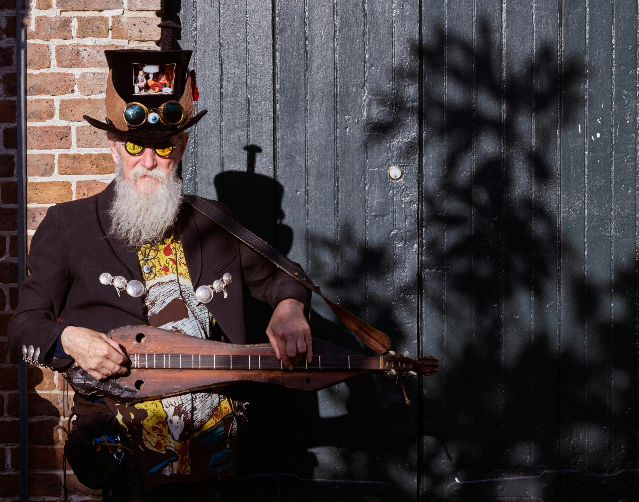 En eldre musiker kledd i en fantasifull drakt, som spiller på et strengeinstrument.