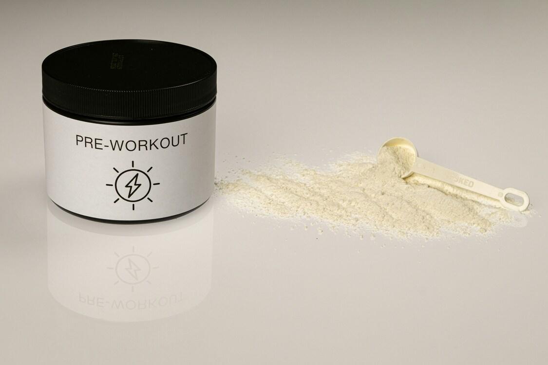 Boks med pre-workout pulver og en måleskje med pulver ved siden av.