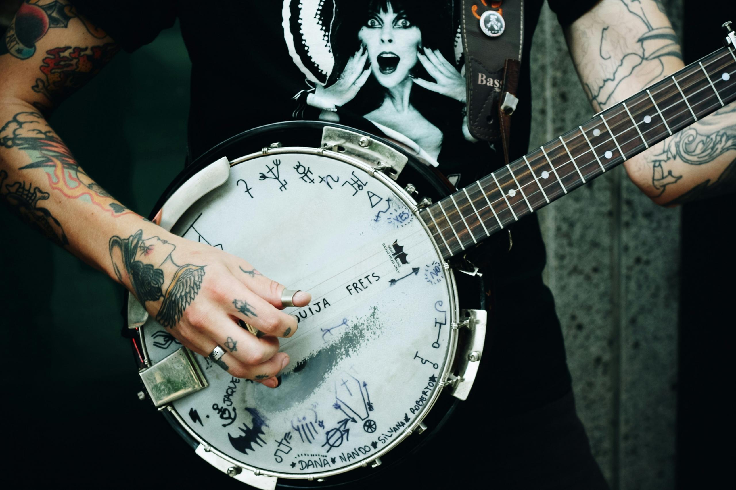 Nærbilde av en tatovert musiker som spiller banjo med et unikt design på instrumentet.