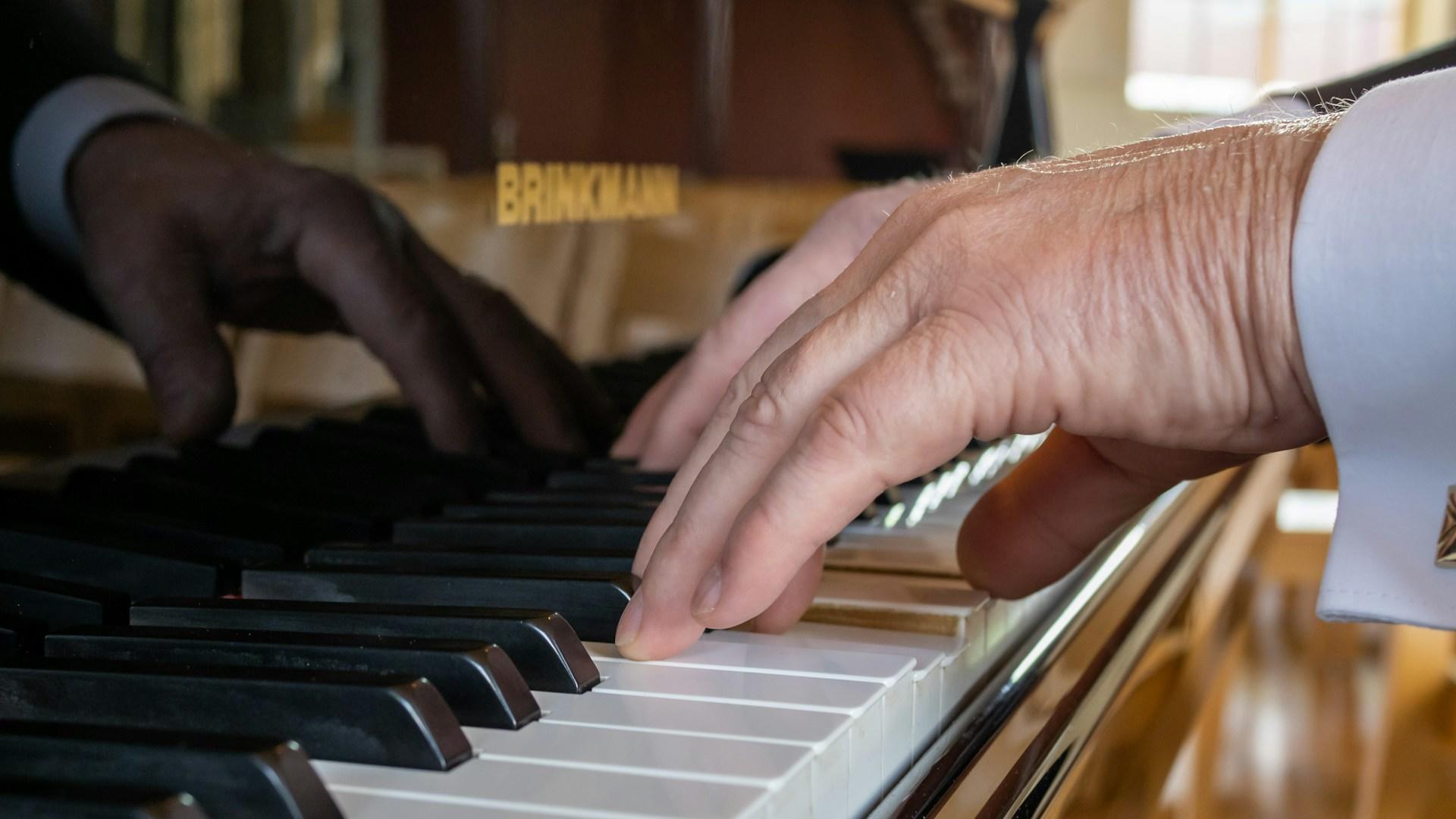 Eldre hender spiller på sort piano.