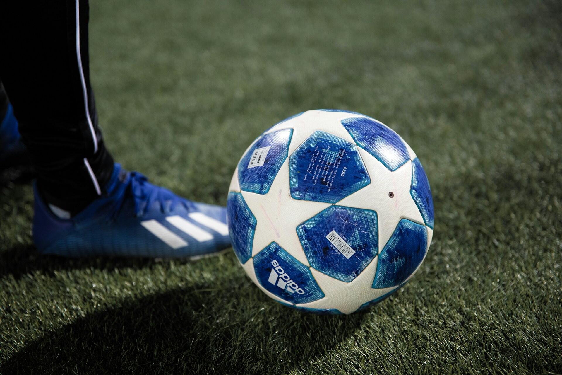 UEFA dorball blått Adidas-mønster og blå fotballsko på kunstgress