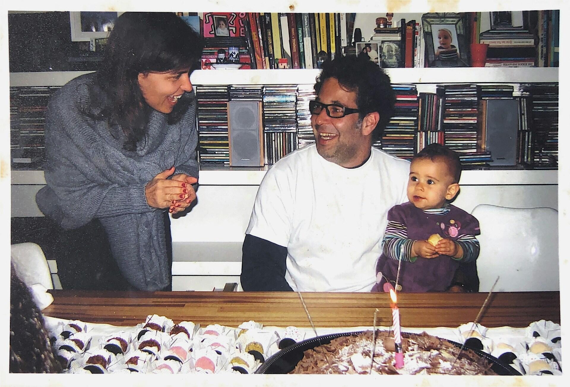 Familie smiler rundt et bursdagsbord mens en kvinne holder tale