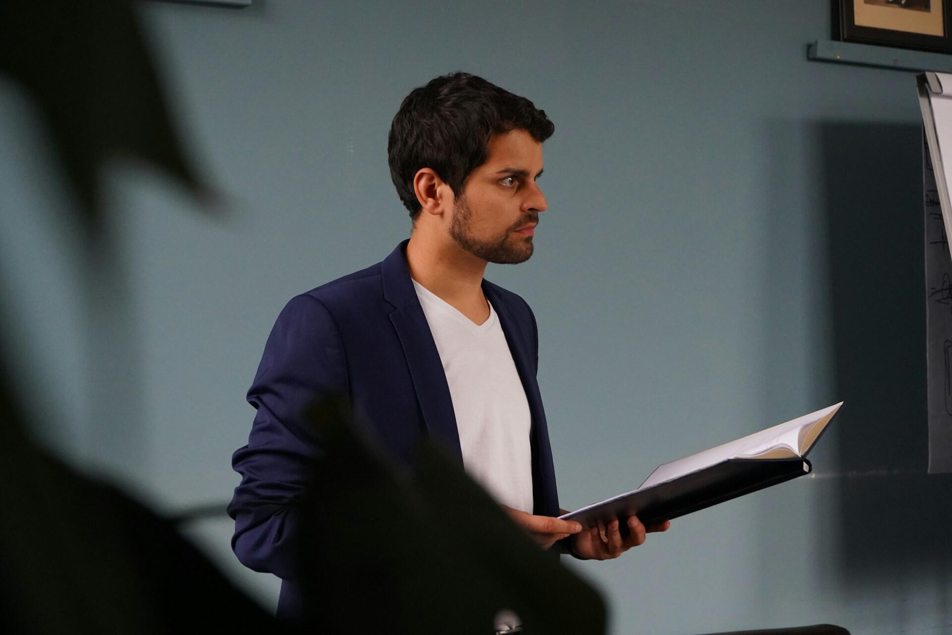 Ung mann holder tale foran en forsamling med et åpent manus i hendene