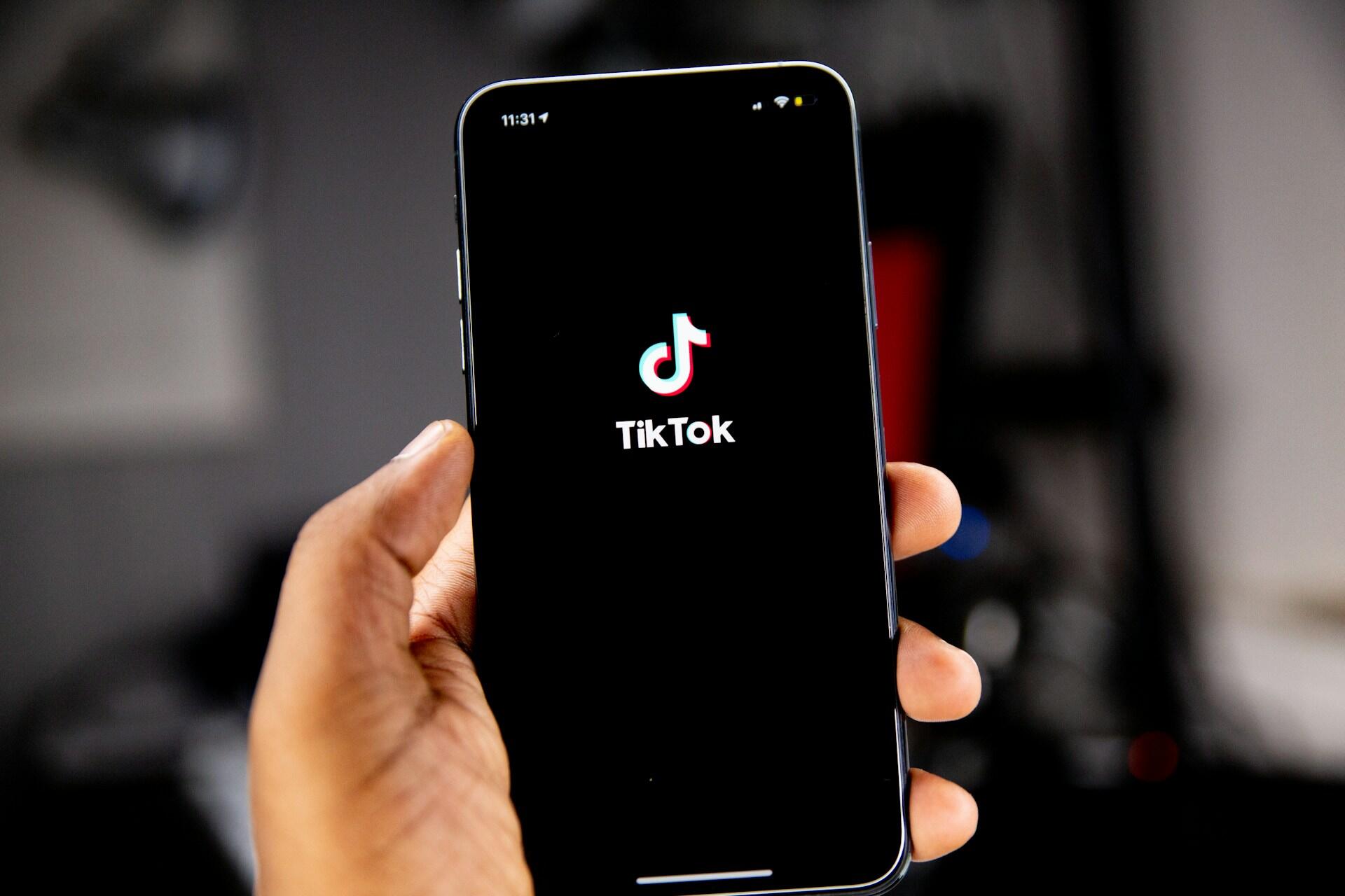Hånd holder sort mobil med TikTok logo.
