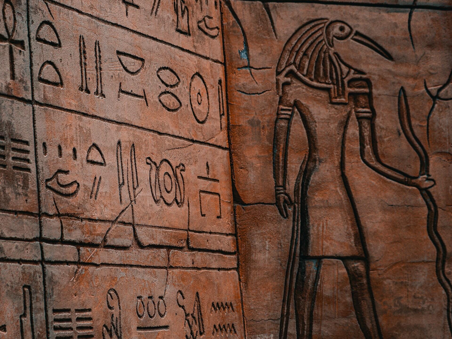 Utskjæringer av hieroglyfer og egyptisk gud med fuglehode på en tempelvegg.
