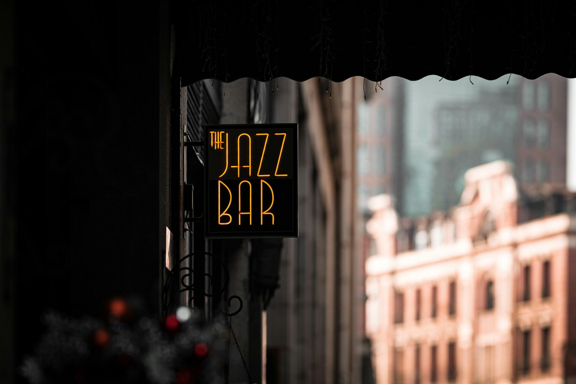 Neonskilt med teksten «The Jazz Bar» henger over en bygate i bakgrunnsbelysning.