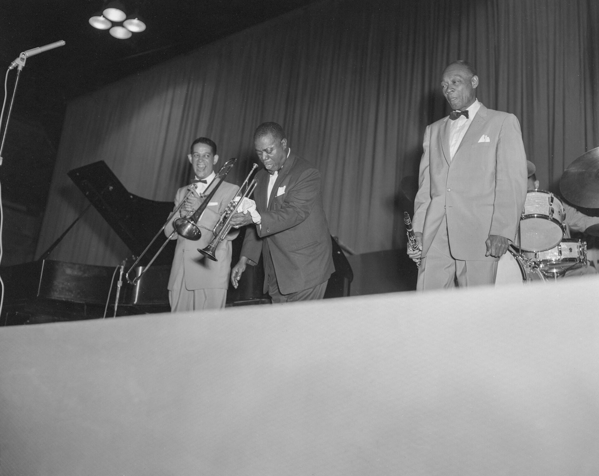 Louis Armstrong spiller trompet sammen med jazzmusikere på scenen i klassiske dresser.