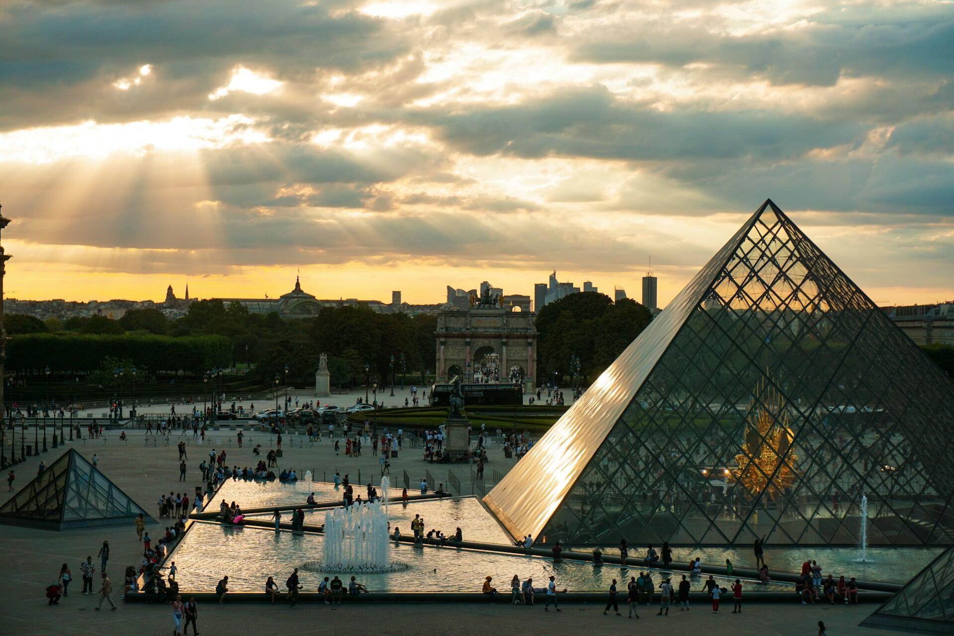 Louvre i Paris med sol som skinner gjennom skyene.