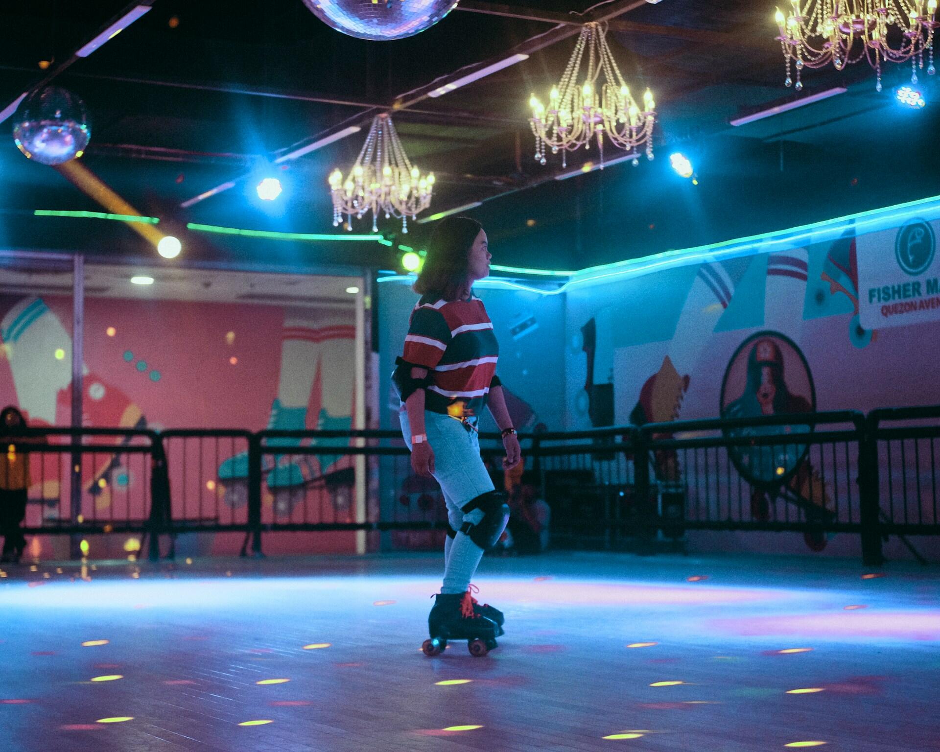 Kvinne som ruller på rulleskøyter i en discoinspirert hall med neonlys og speilkuler.