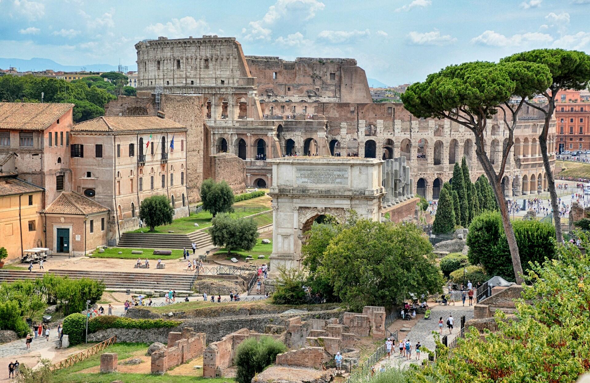 Romerske ruiner blant trærne i Roma sentrum med Colosseum i bakgrunnen.