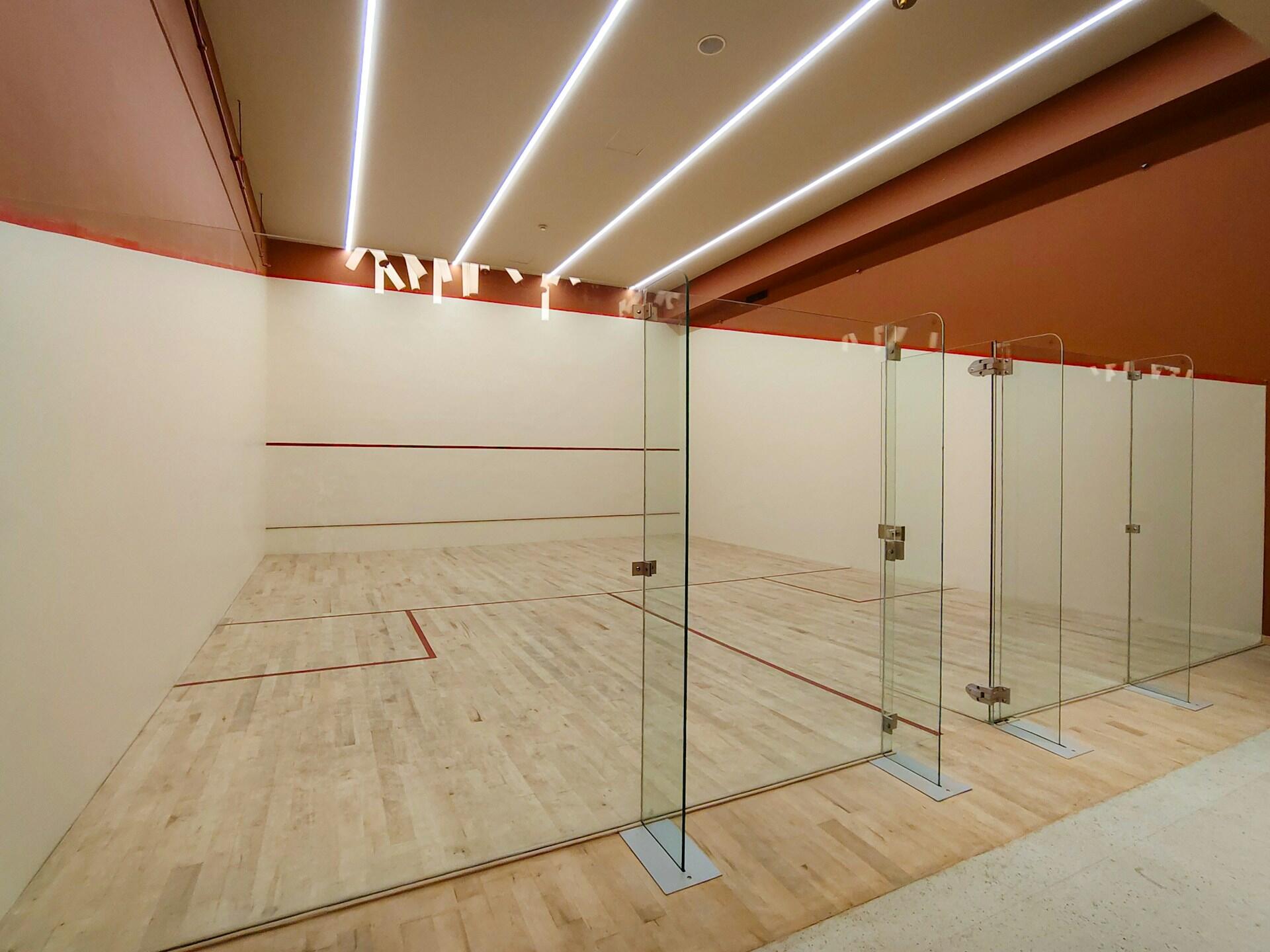 Moderne squashbane med glassvegger og lyst tregulv, sett uten spillere.