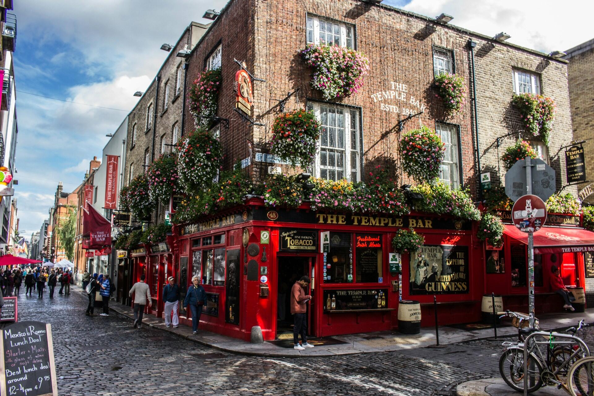 Fargerikt gatebilde av Temple Bar i Dublin, med folk og blomsterpyntet fasade