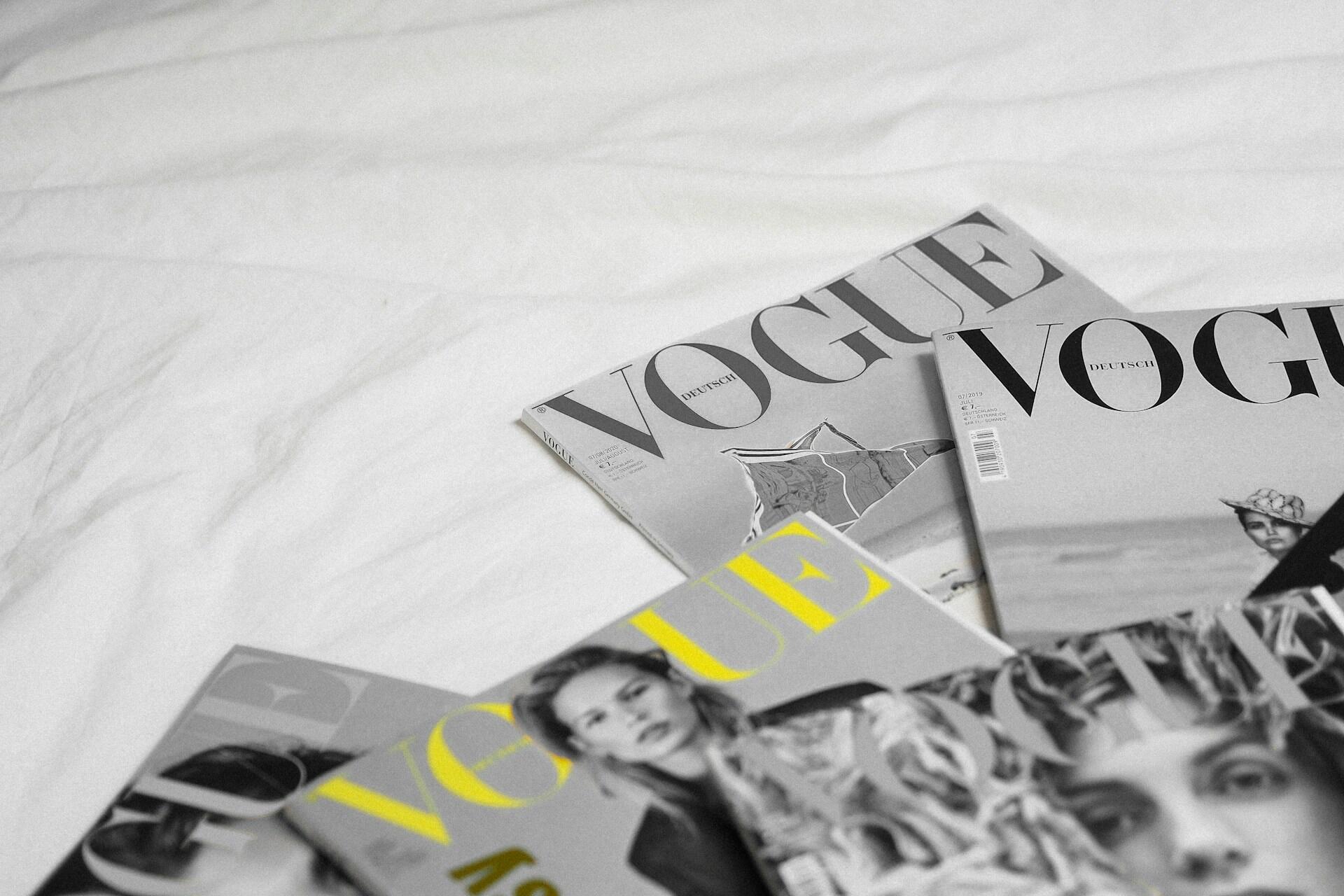 Vogue-magasiner ligger spredt på en seng med hvitt laken.