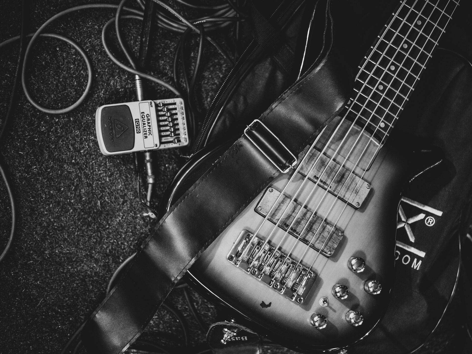 Elgitar liggende på gulvet sammen med ledninger og en grafisk equalizer-pedal.