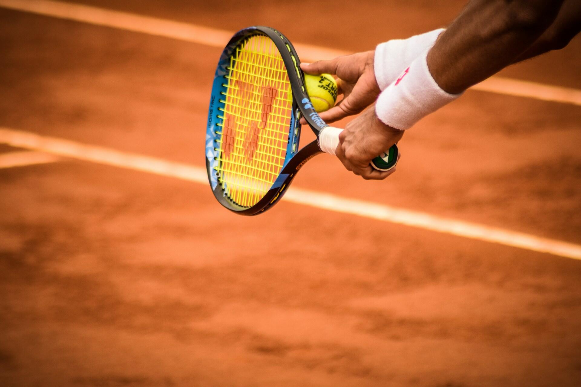 Armer holder en gul tennisracket og står klar for å serve med ball i ene hånda