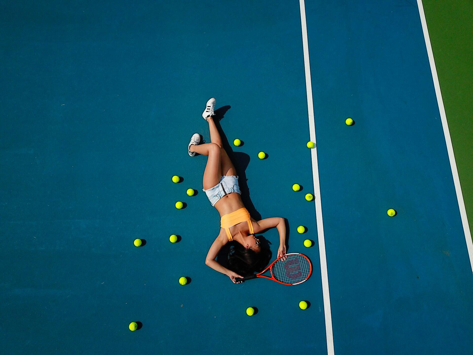 Kvinne som ligger avslappet på tennisbane omgitt av tennisballer