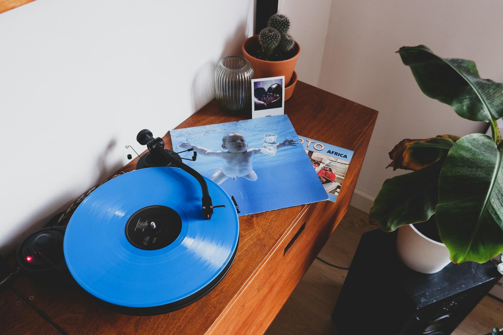 Blå vinylplate og Nirvana-albumet Nevermind på en trebenk ved siden av en potteplante.