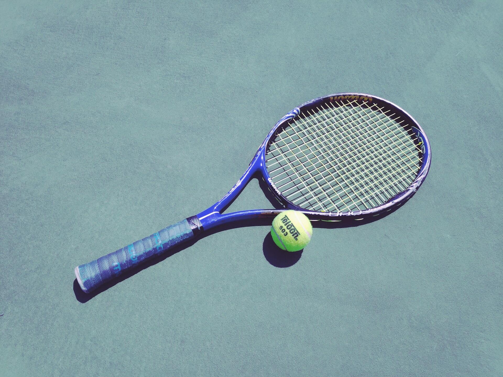 Blå tennisracket og grønn tennisball liggende på underlaget.