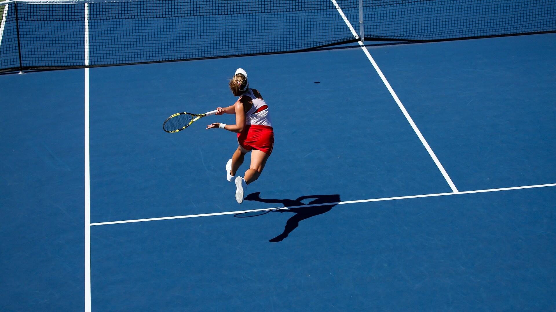 Dame med rødt skjørt og hvit topp løper på tennisbanen