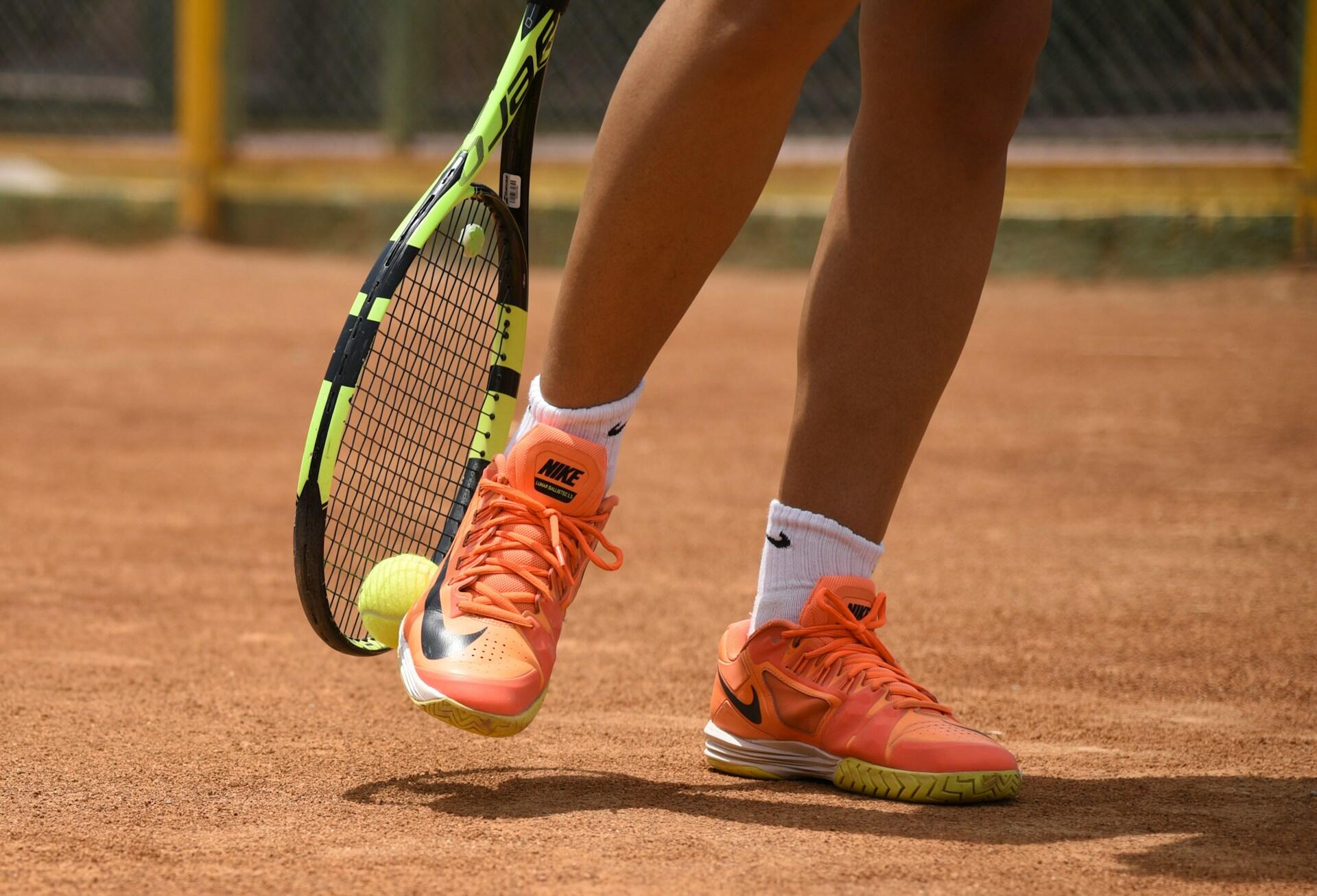 Tennisspiller med oransje sko spretter tennisball med racketen