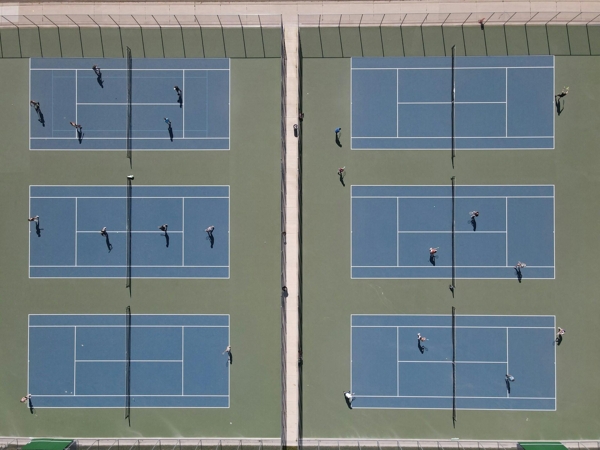 Luftfoto av seks tennisbaner med spillere i aksjo
