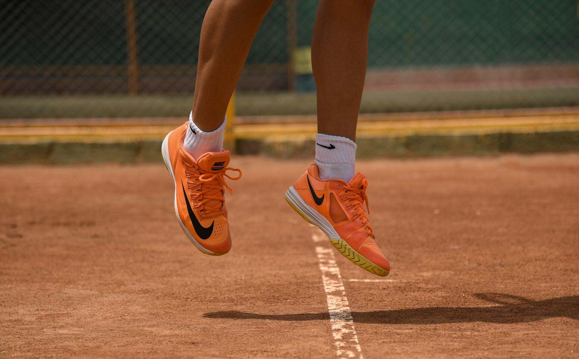 Tennisspiller med oransje sko i et hopp over grusbanen.