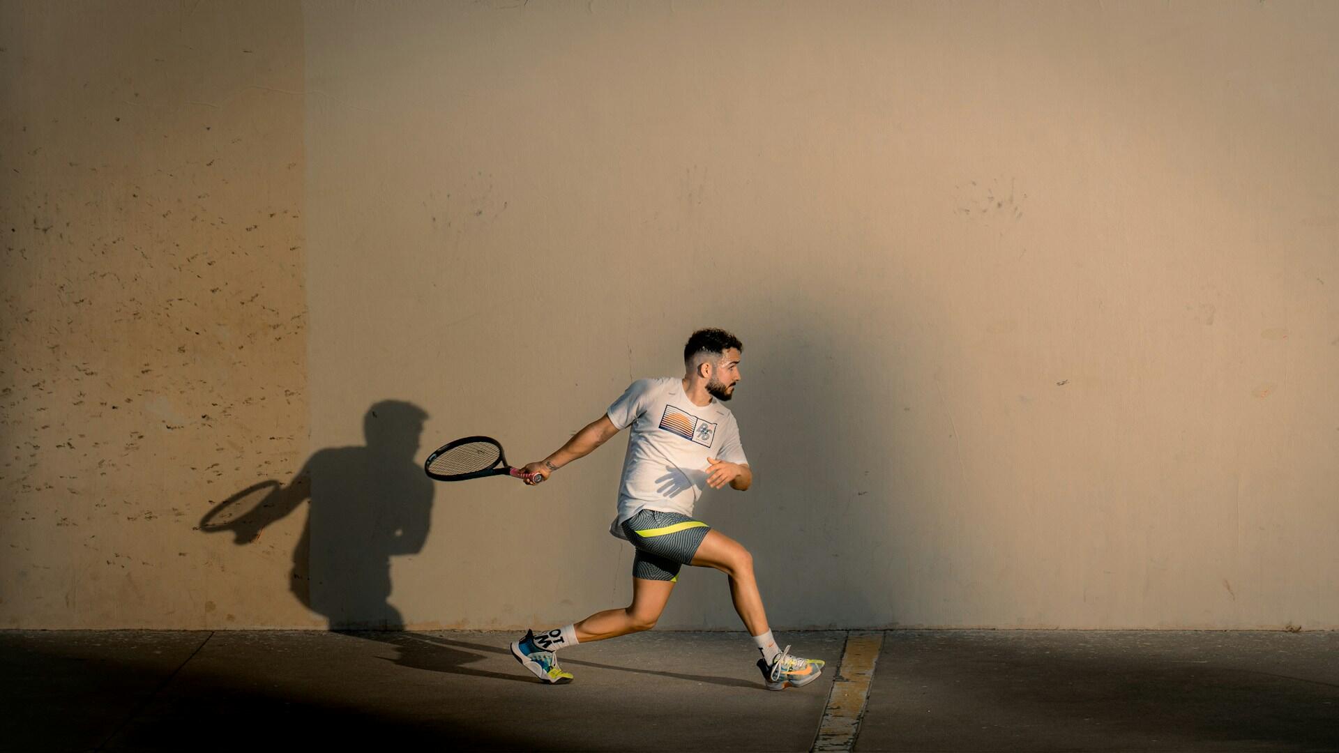 Tennisspiller som slår ballen mot en vegg i sollys
