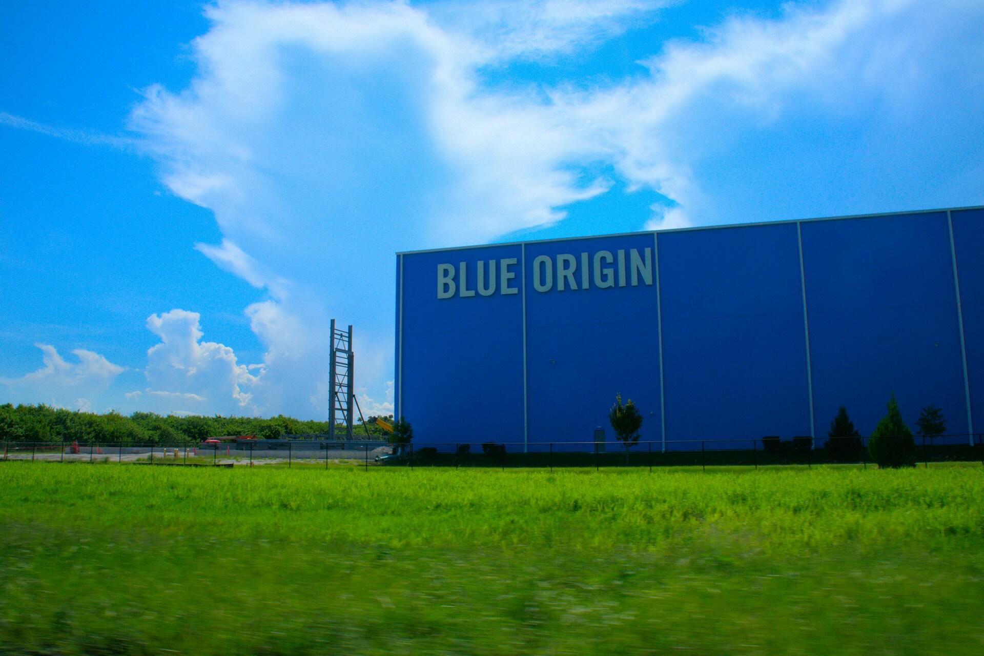Blue Origin sitt blå industribygg med firmalogo på fasaden og grønt gress i forgrunnen