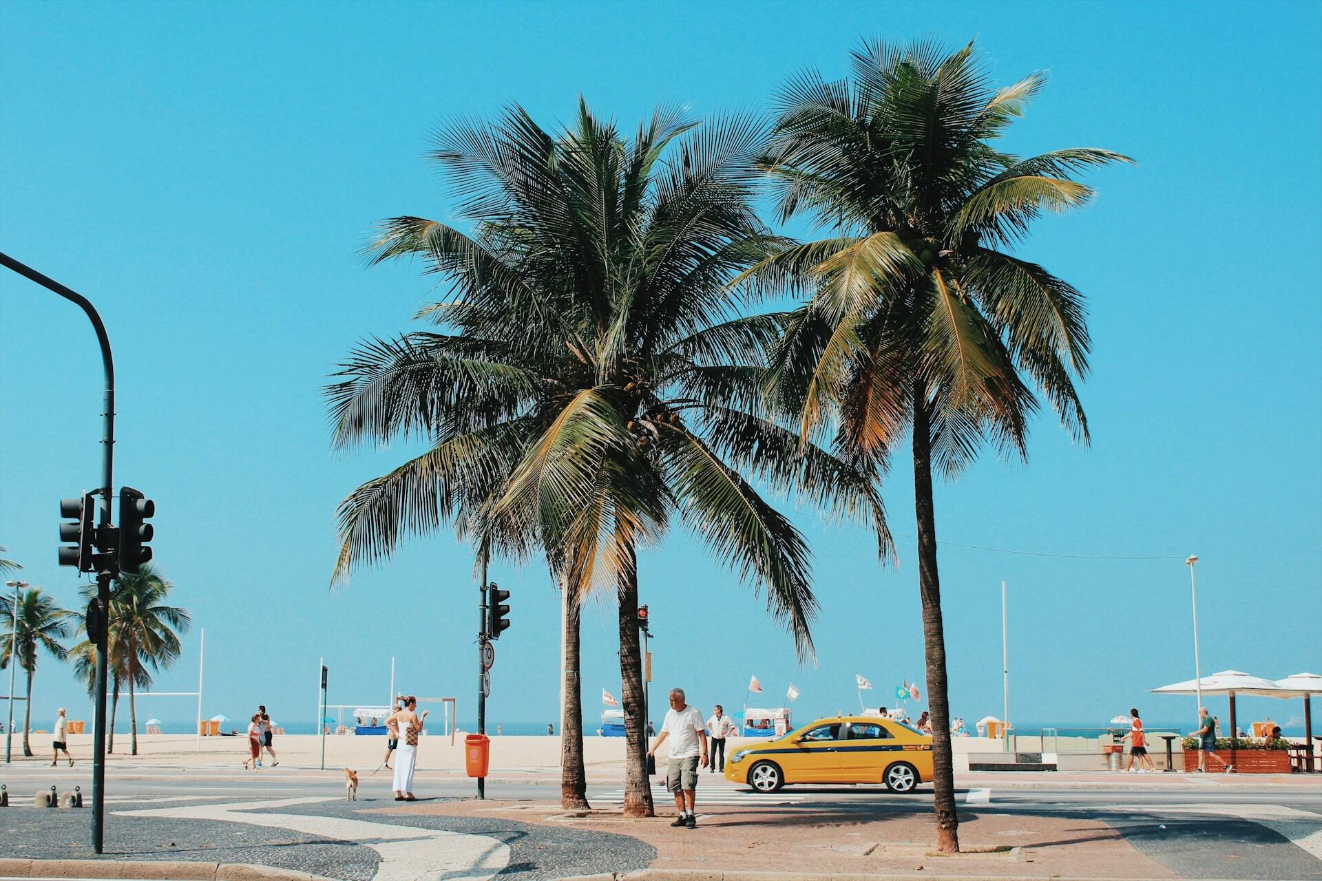 Strandpromenade i Brasil med palmer, gul bil og mennesker som går langs den berømte bølgemønstrete fortauet