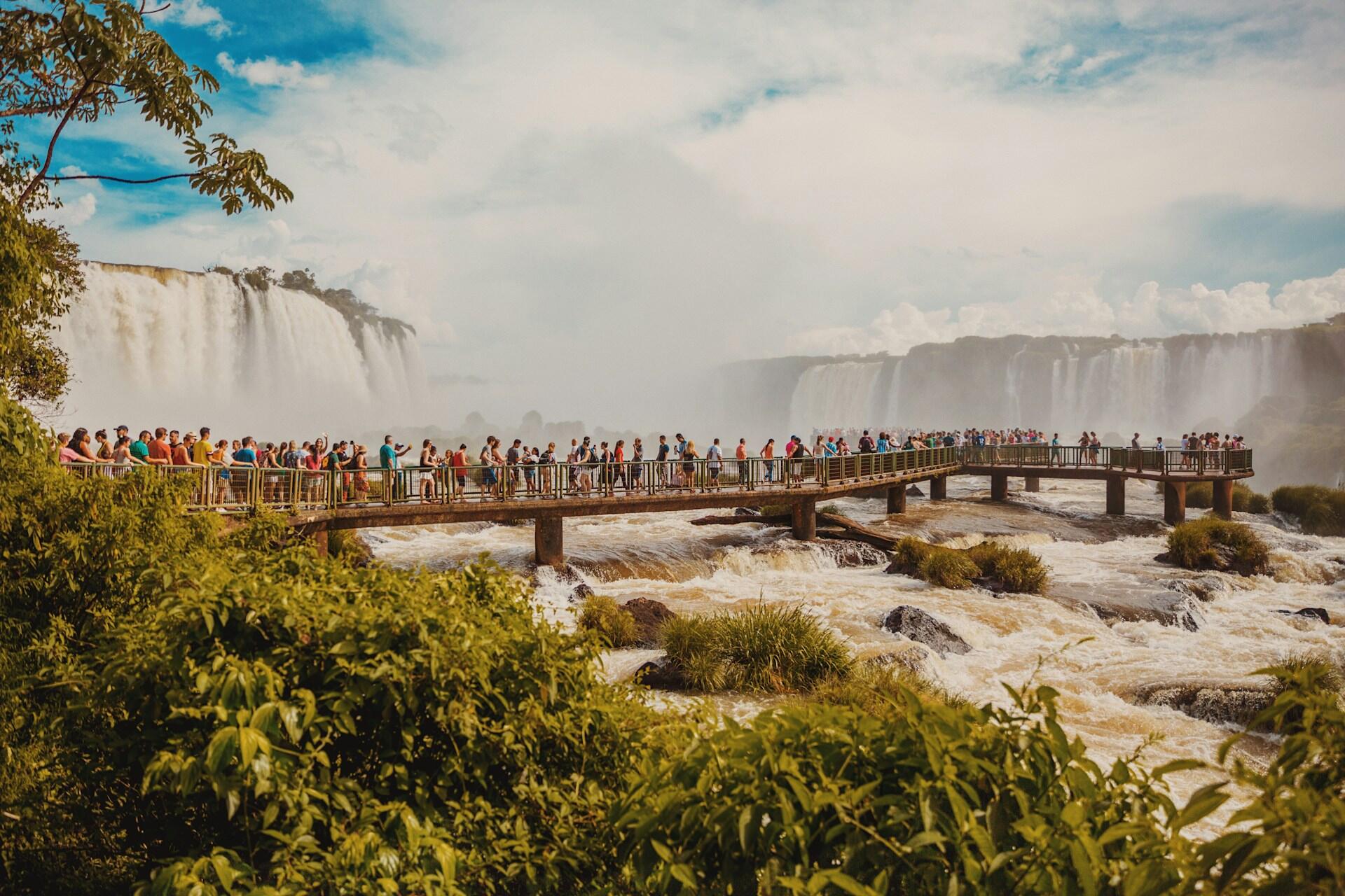 Turister på utsiktsplattform ved Iguazu-fossene i Brasil med kraftige fossefall i bakgrunnen