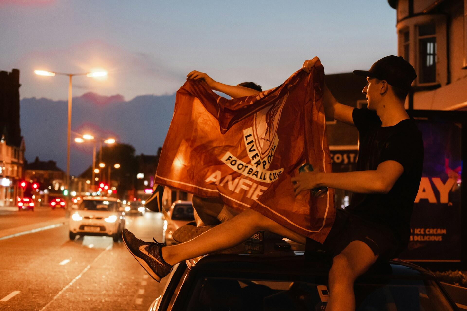 Liverpool-fans sitter på taket av bil med flagg.