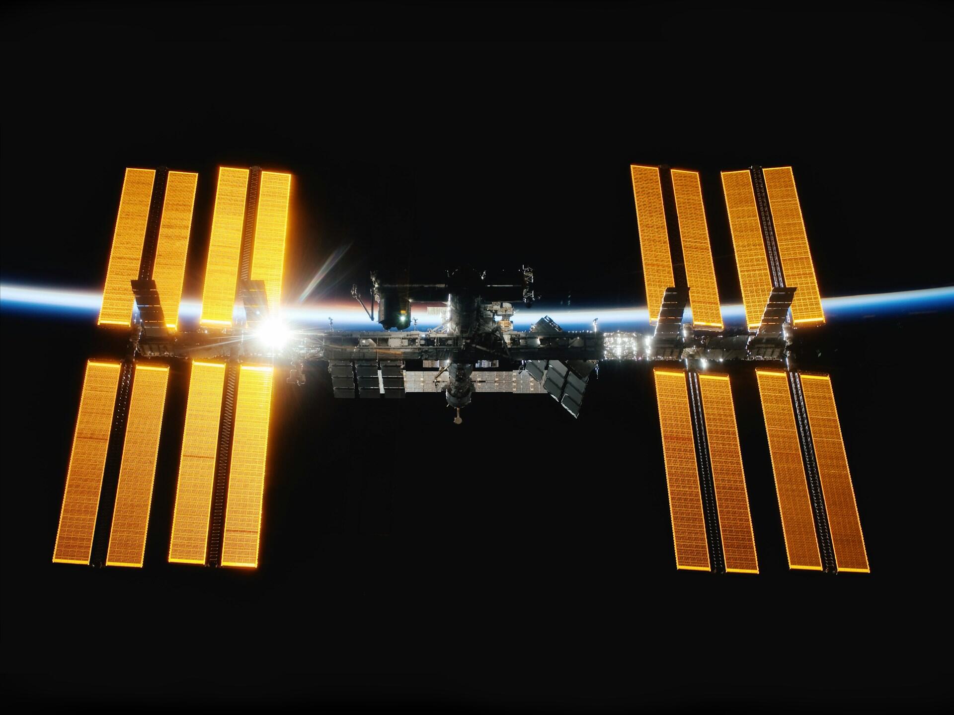 Den internasjonale romstasjonen ISS med gylne solpaneler mot jordens blå atmosfære