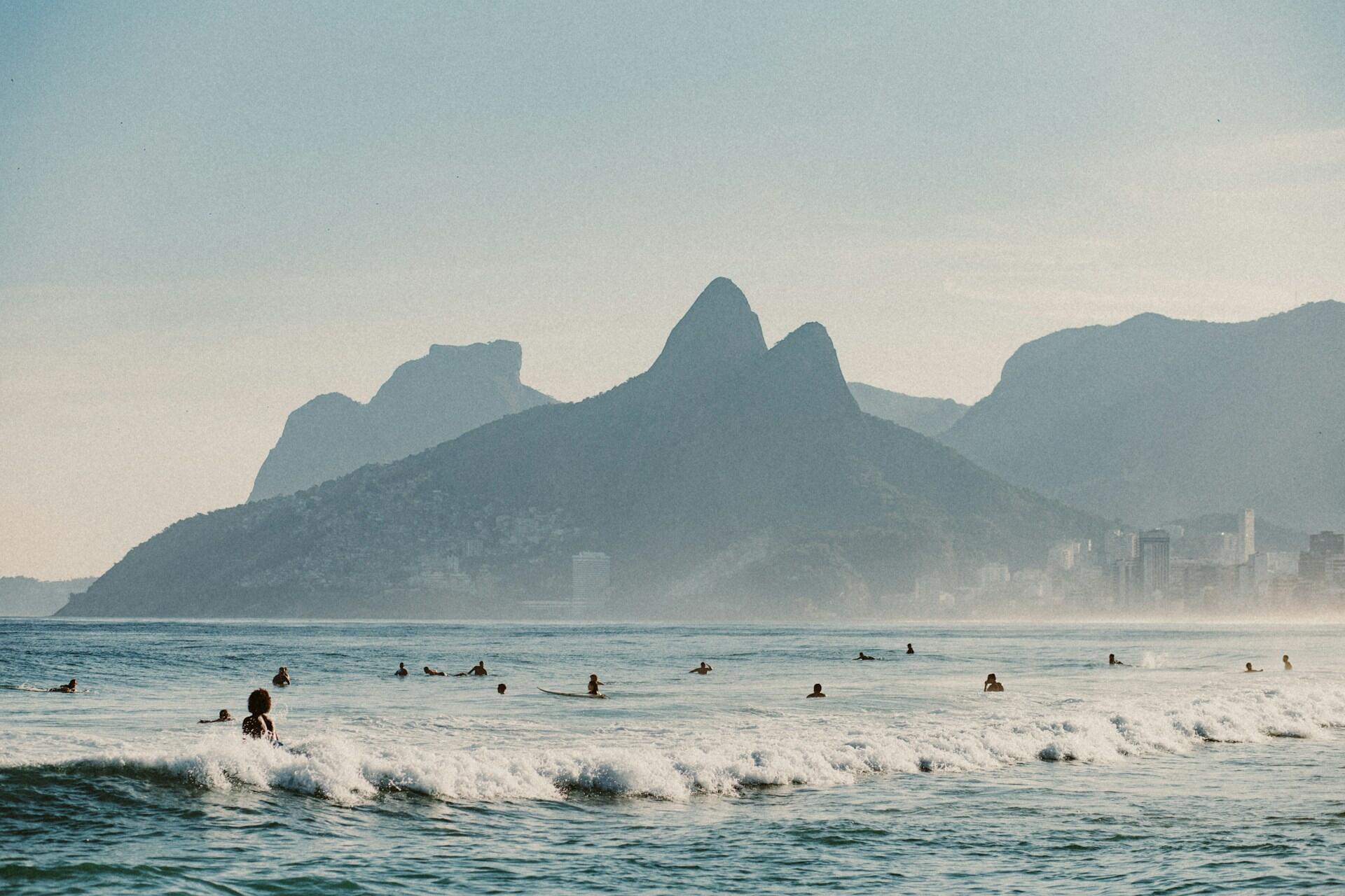 Folk bader i havet ved Ipanema strand i Rio de Janeiro med fjell i bakgrunnen ved solnedgang