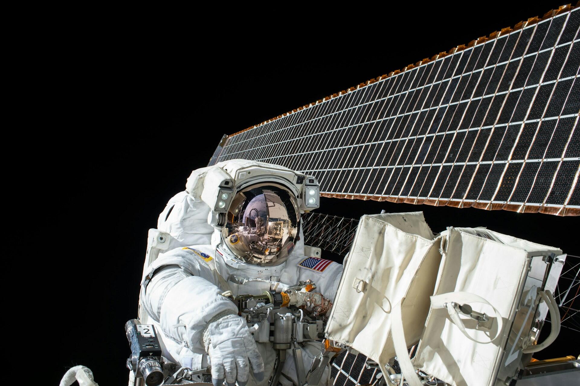 Astronaut i hvit romdrakt utfører romvandring utenfor den internasjonale romstasjonen