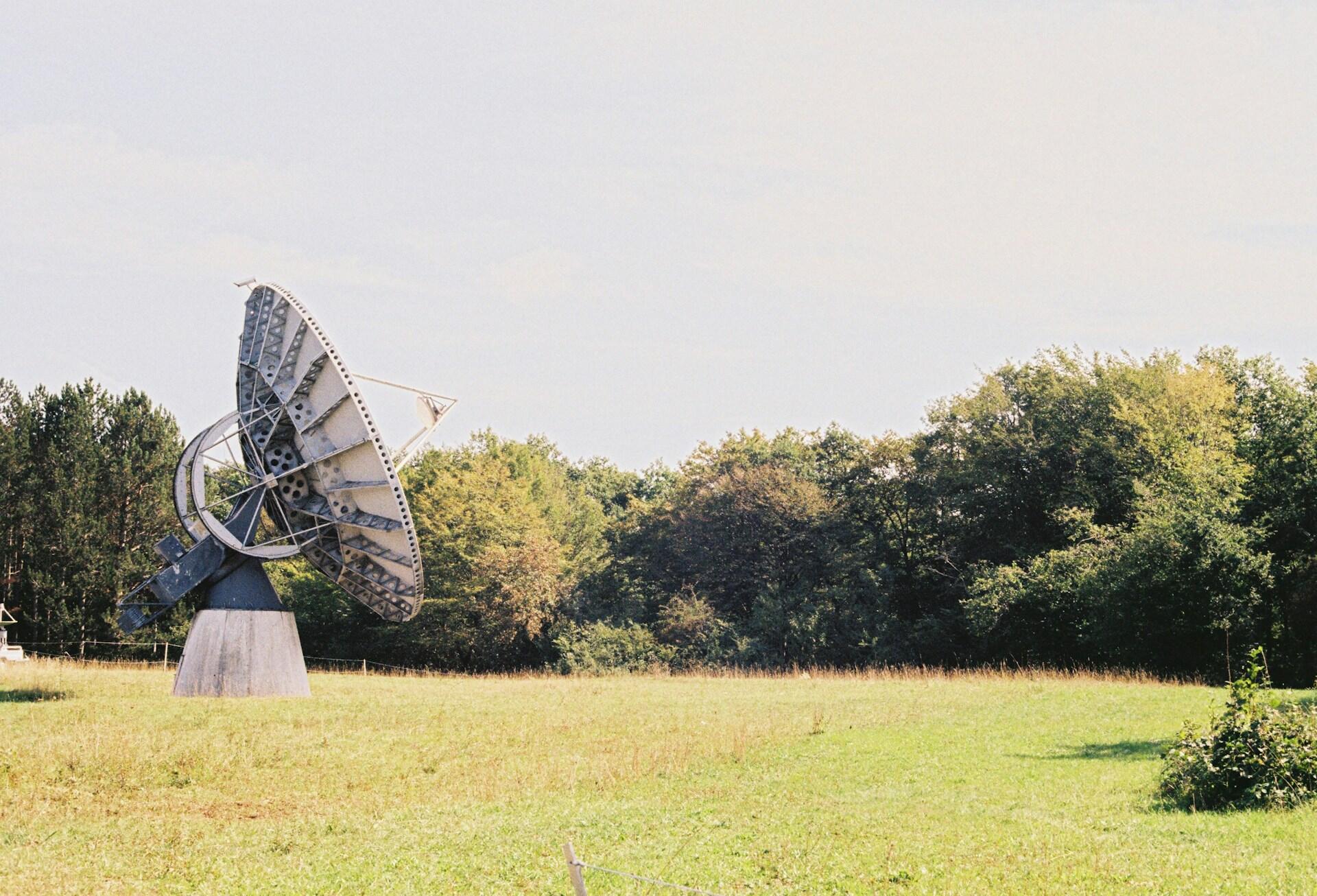 Stor satellittantenne i landlig område omgitt av grønne trær og eng