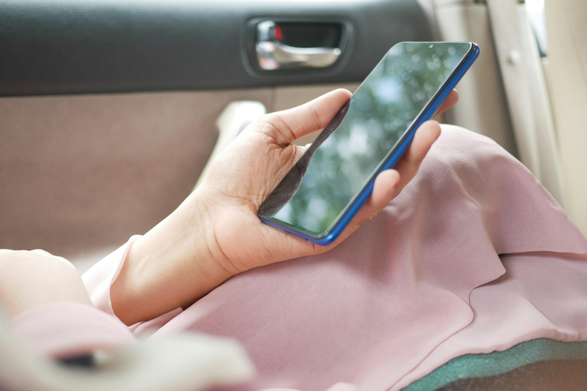 Persons hender som holder en blå smarttelefon i bil