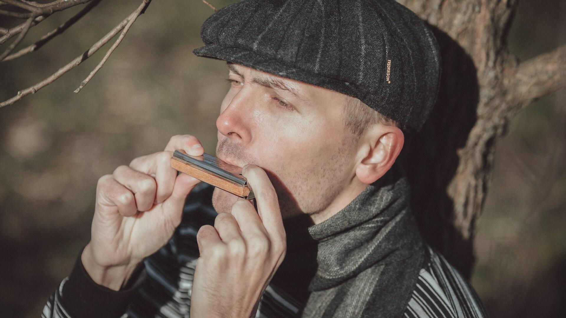 Mann som spiller munnspill i dagslys, et klassisk bluesinstrument.