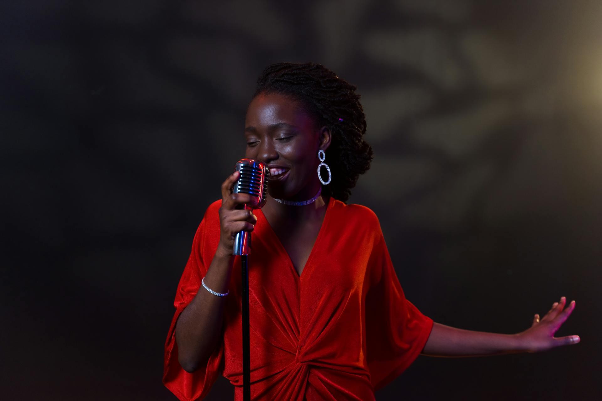 Kvinne i rød kjole synger blues med vintage mikrofon på scenen.
