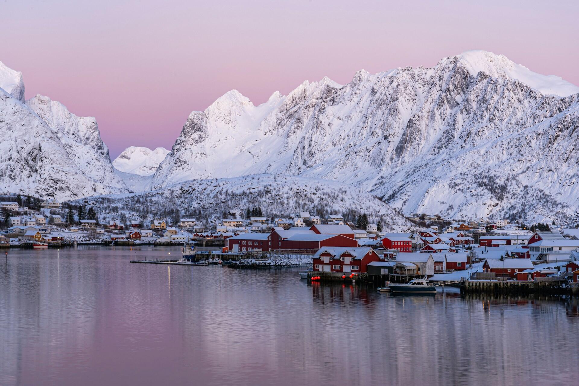 Lofoten med snødekte fjell og tak og rosa himmel bak
