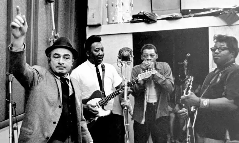 Muddy Waters spiller gitar i studio sammen med Phil Chess og bandmedlemmer under innspilling.