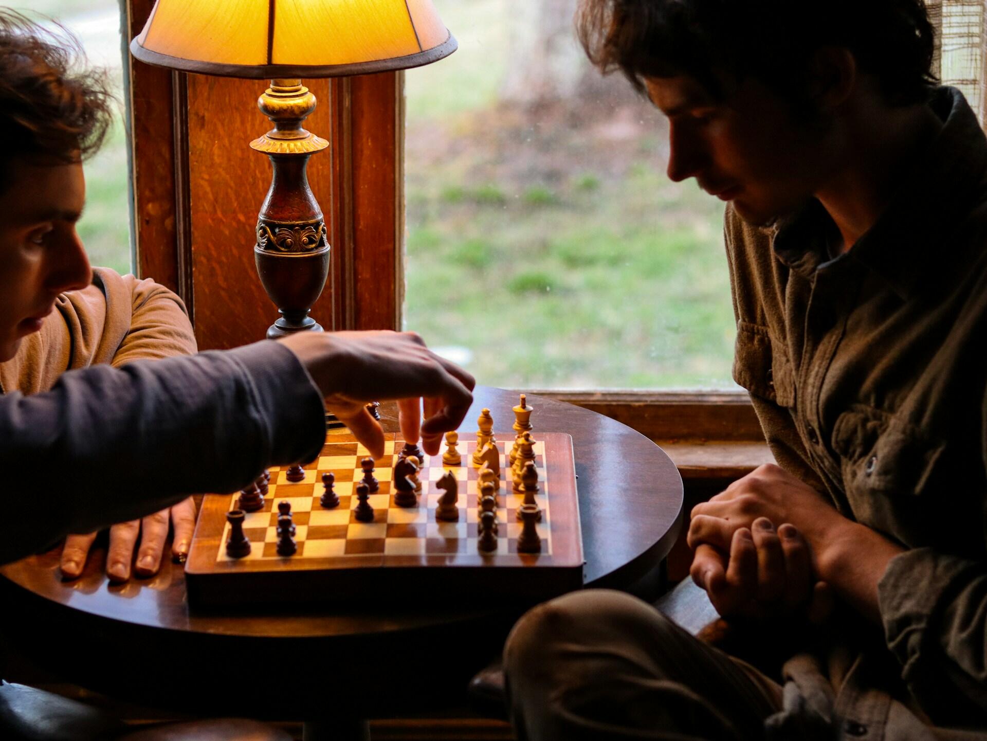 To personer spiller sjakk ved et bord mens den ene flytter en bonde, som illustrerer hvordan sjakk bonde trekk brukes i praksis.