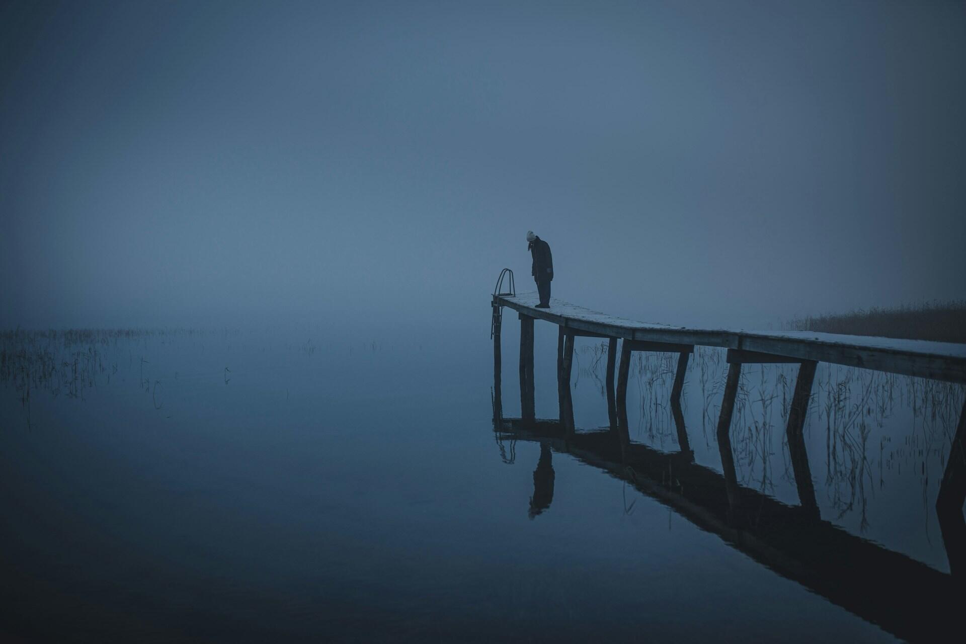 Person står på brygge ved stille vann i tett tåke