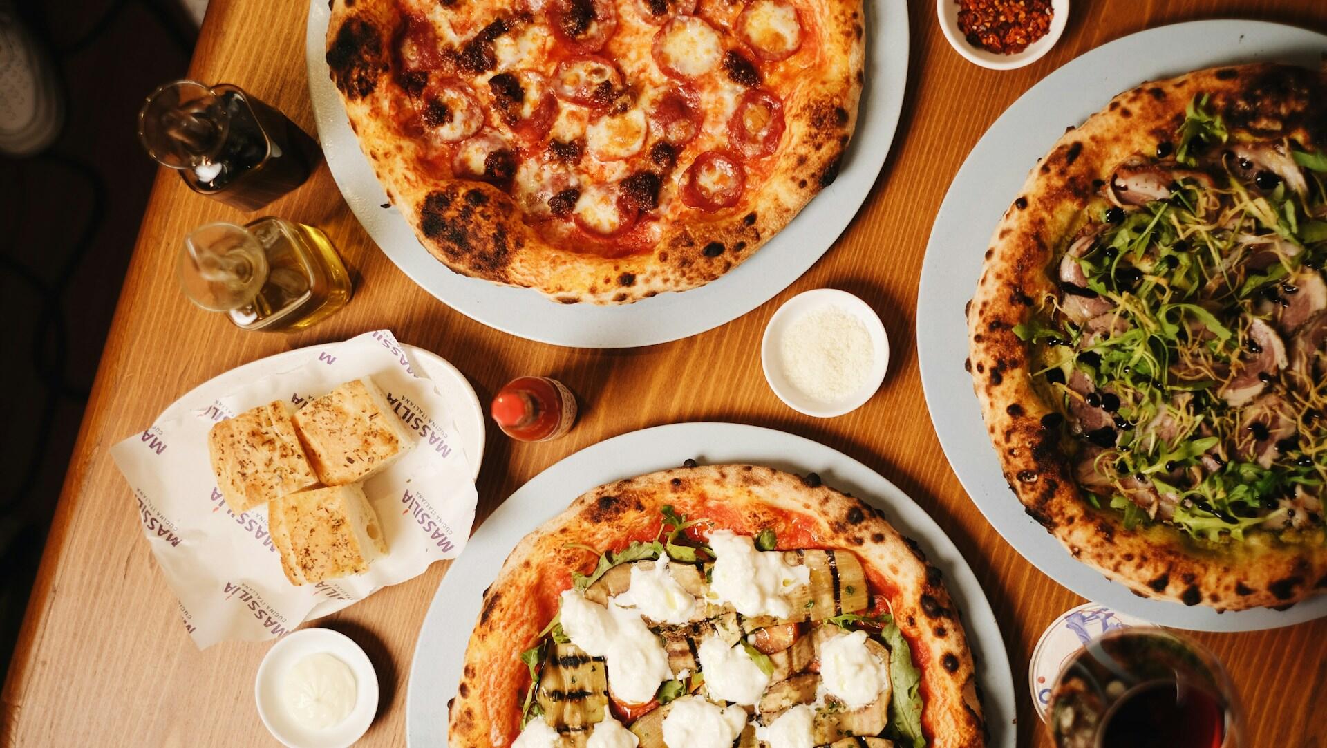 Ulike pizzaer står på et bord sammen med diverse tilbehør