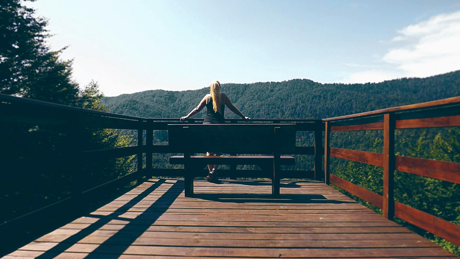 Person som sitter på en treplatting og ser utover en grønn fjellside med skog – perfekt utsiktspunkt for å studere natur til tegning