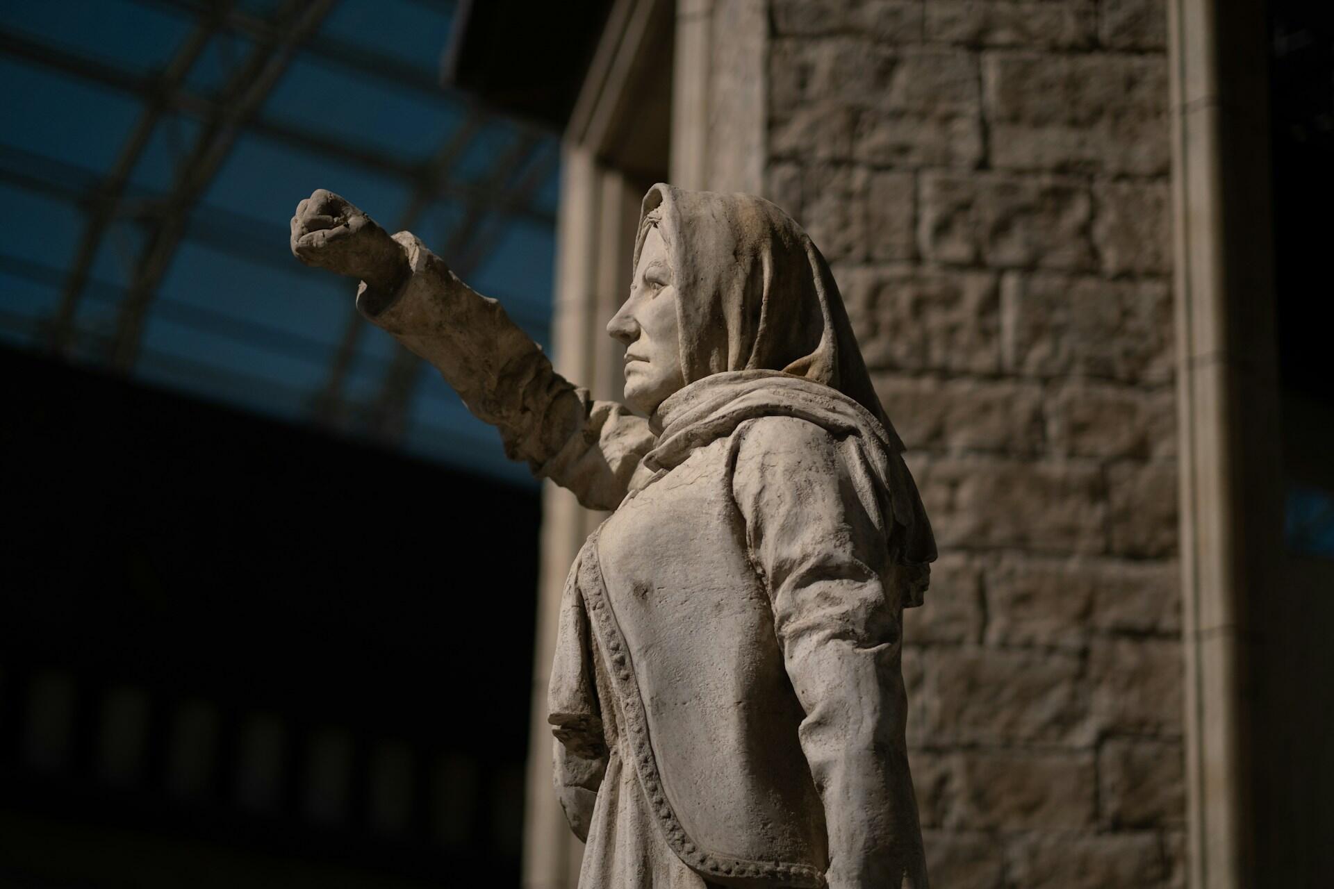 Statue av en kvinne med knyttet neve løftet i været foran en steinbygning