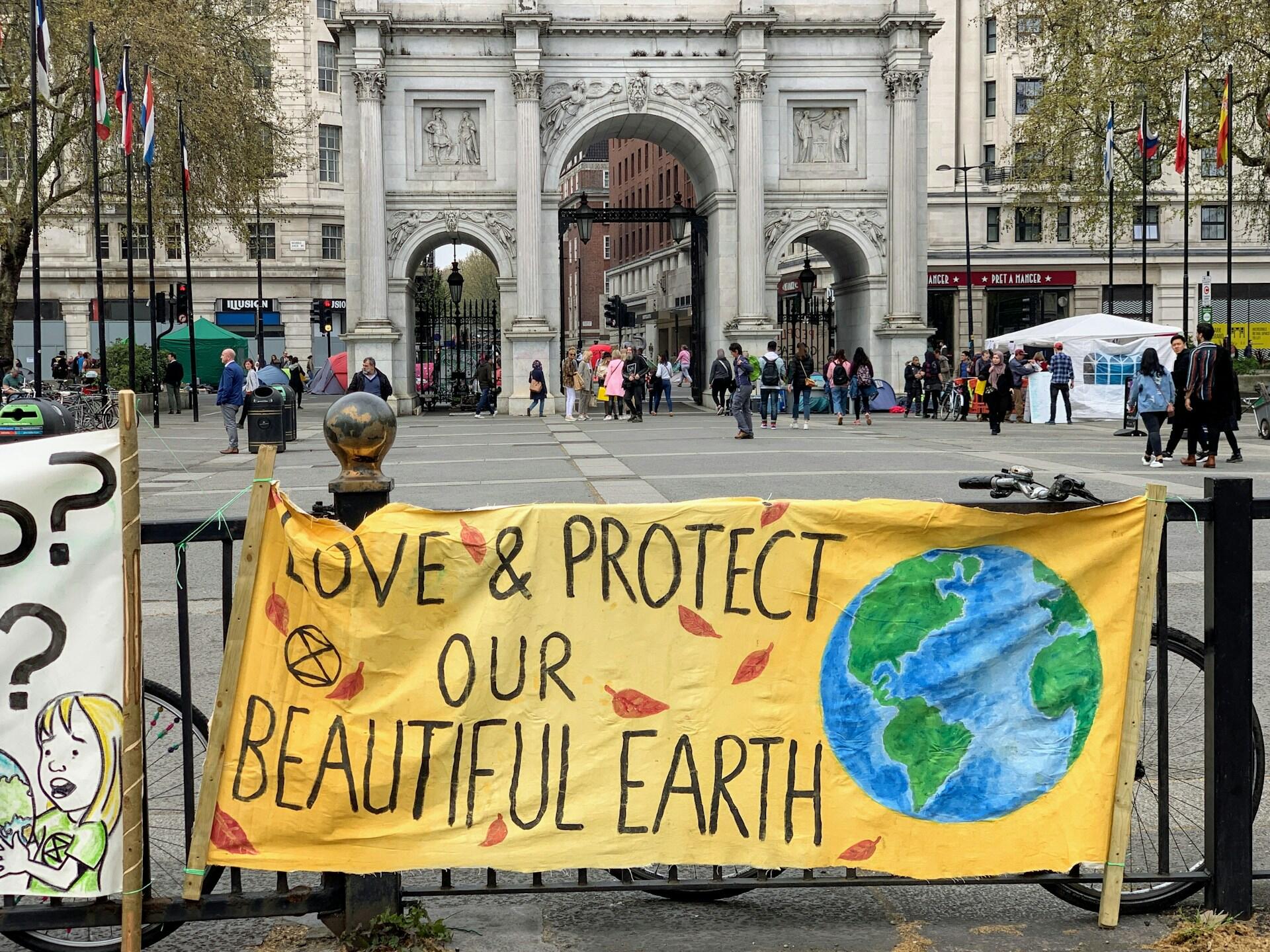 Gult banner festet til et gjerde med teksten «Love and protect our beautiful earth» foran en klassisk bybygning i London