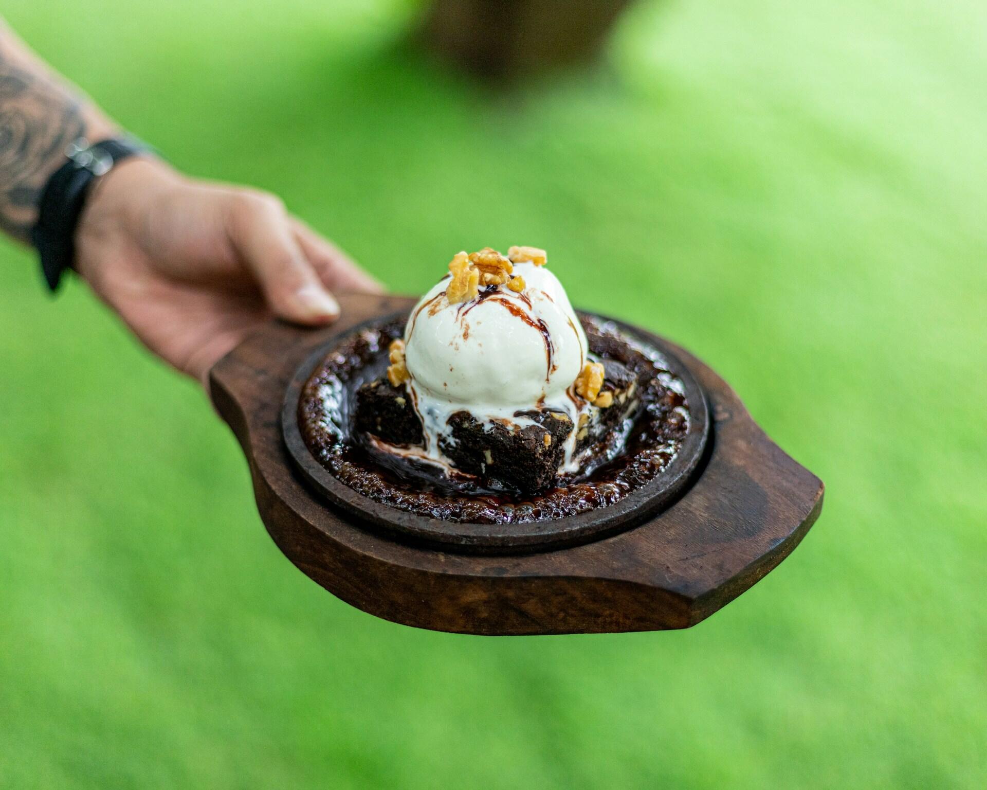 Grillet brownie i støpejernspanne servert med vaniljeis og nøtter som varm dessert på grill.